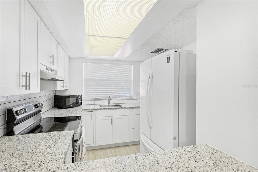 2300 Stickney Point Road, Unit 102 Sarasota, FL 34231 - Photo 8 of 32 a kitchen with stainless steel appliances kitchen island granite countertop a refrigerator and a sink