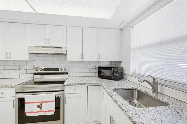 a kitchen with granite countertop white cabinets a sink and stainless steel appliances
