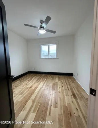 an empty room with wooden floor a ceiling fan and window