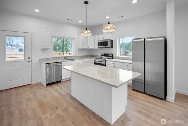 a kitchen with stainless steel appliances granite countertop a sink a stove a refrigerator and island with wooden floor