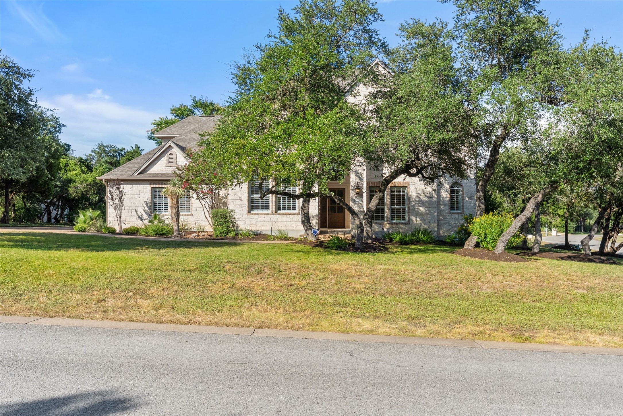 8215 Dark Ridge Cove Austin, TX 78737 - Photo 3 of 40 8215 Dark Ridge Cove features a classic Texas stone facade with shuttered windows and timeless elegance amidst mature shade trees.