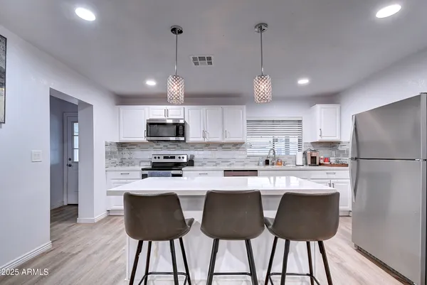 a kitchen with stainless steel appliances granite countertop a dining table chairs refrigerator and cabinets