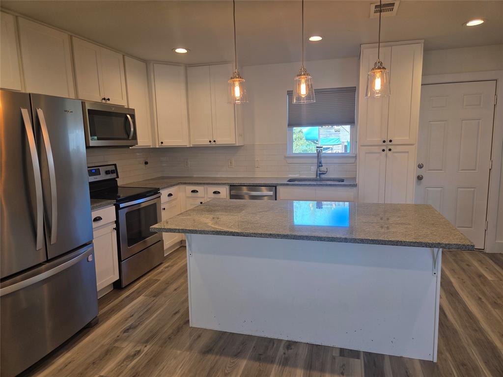 482 Trout Street Rockwall, TX 75032 - Photo 1 of 20 Kitchen with stainless steel appliances, dark stone counters, white cabinetry, decorative light fixtures, and a center island