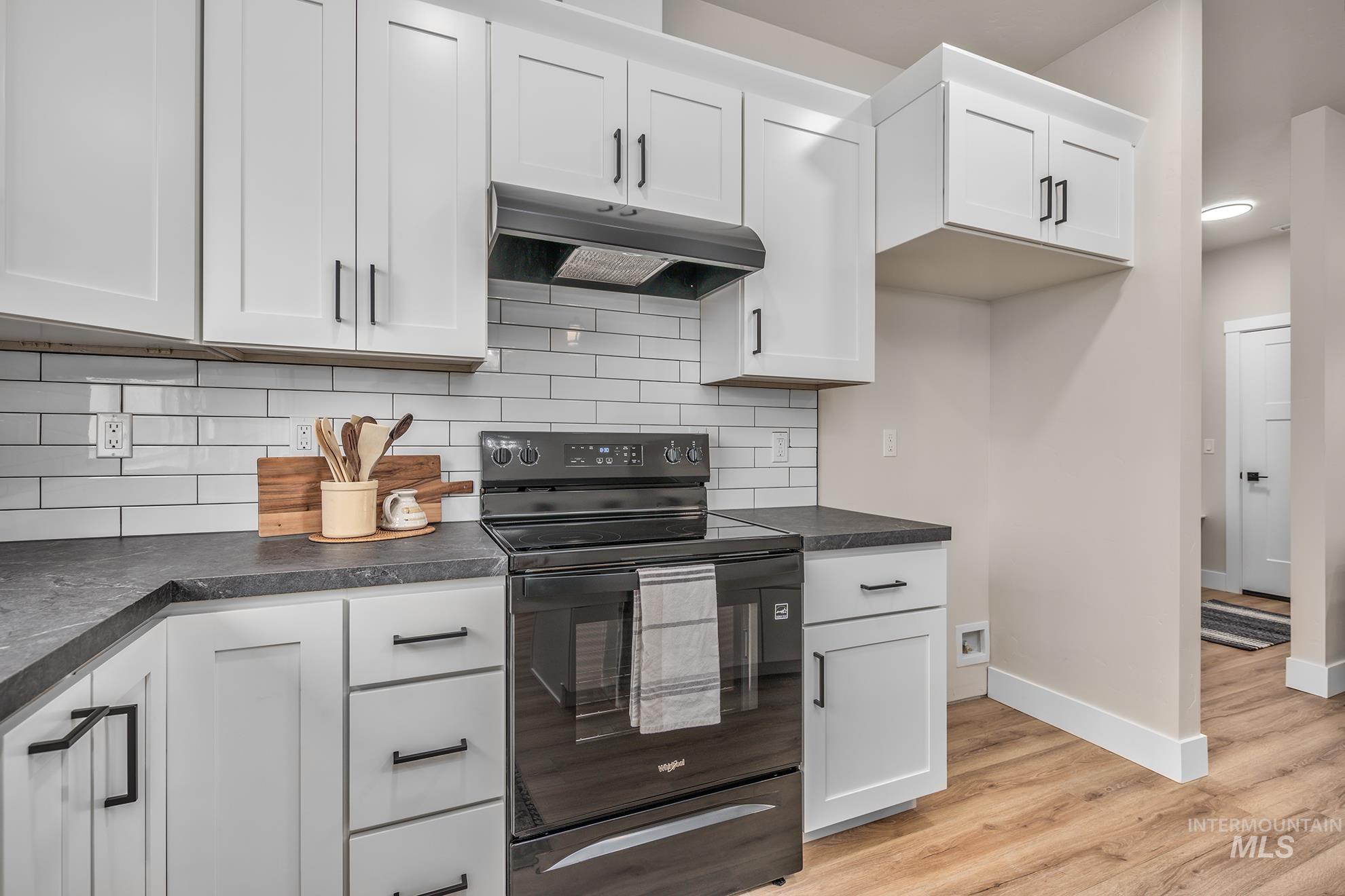 1367 Hansen Road Weiser, ID 83672 - Photo 10 of 36 Kitchen featuring black range with electric cooktop, dark countertops, decorative backsplash, and white cabinetry