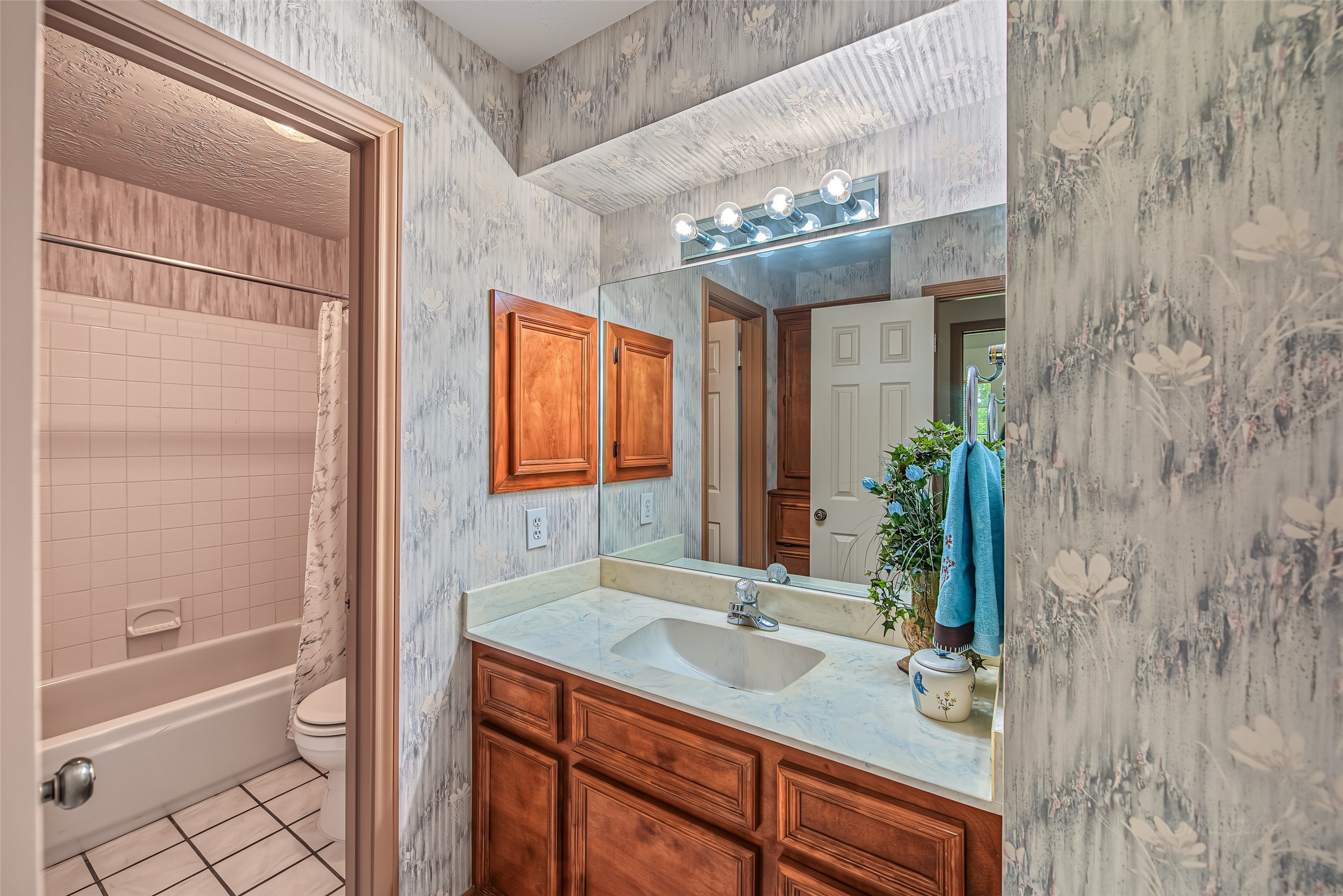 1345 Peach Ridge Road Brookshire, TX 77423 - Photo 36 of 50 This well-designed secondary bathroom features a functional split-vanity layout that separates the primary grooming space from the tub and toilet area. The vanity zone offers a solid wood vanity with raised-panel cabinetry, a light marble-look countertop with an undermount sink, a large wall-to-wall mirror, and overhead vanity strip lighting.