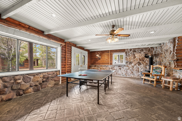 4725 Pine Ridge Road Evanston, UT 82930 - Photo 23 of 82 Spacious recreational room featuring a wood-planked ceiling with exposed beams, stamped concrete flooring, extensive window banks, rustic log walls, and a stone accent wall