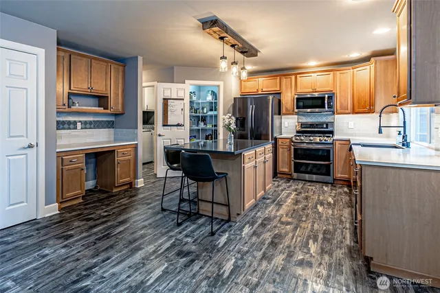 a kitchen with stainless steel appliances a stove top oven a sink dishwasher a dining table and chairs with wooden floor