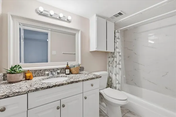 a bathroom with a granite countertop sink a toilet a mirror a vanity a bathtub and shower