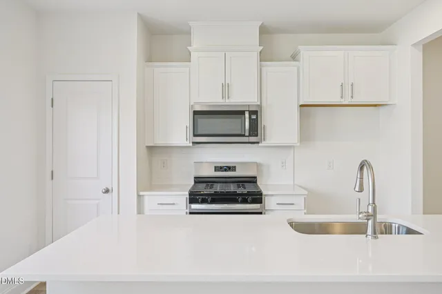 a kitchen with stainless steel appliances a stove a sink a refrigerator white cabinets and wooden floor