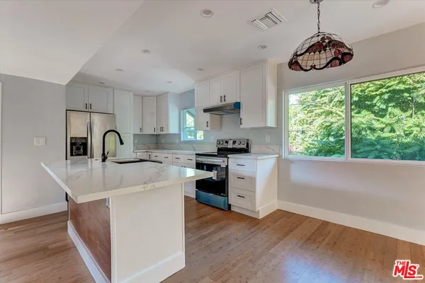 a kitchen with kitchen island a sink a stove a refrigerator cabinets and a wooden floor