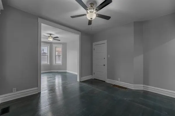 an empty room with wooden floor chandelier fan and windows