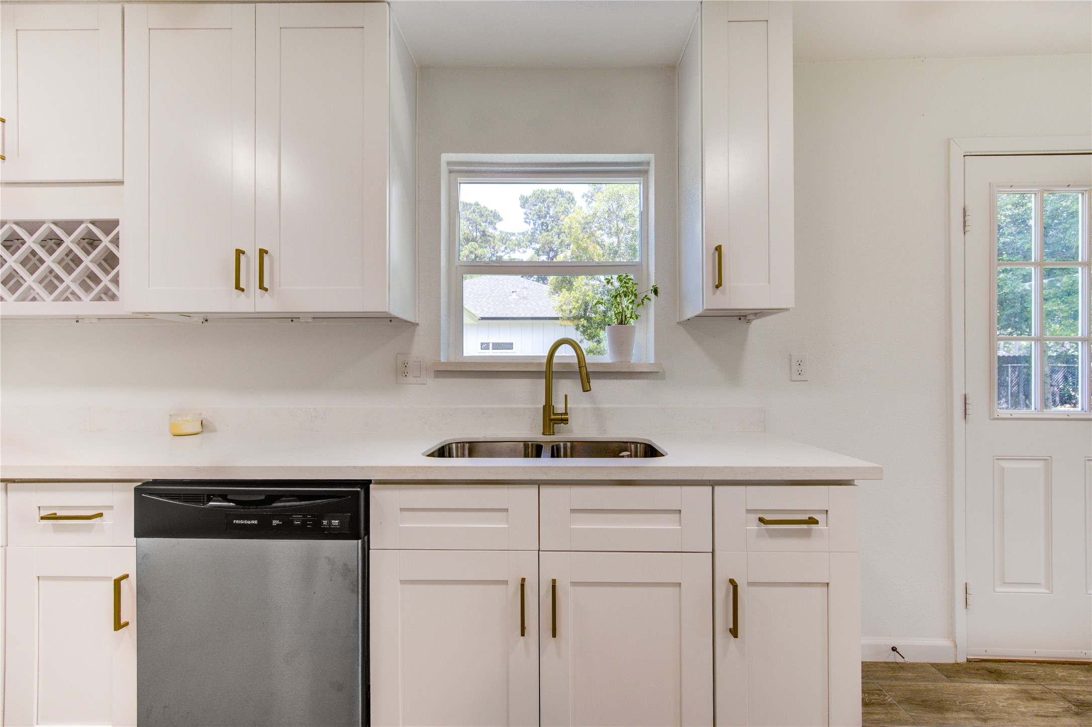 5411 Logston Lane Spring, TX 77389 - Photo 17 of 50 Bright and modern kitchen featuring sleek white cabinetry, a stylish brass faucet, and a built-in wine rack, complemented by stainless steel appliances and a window view.