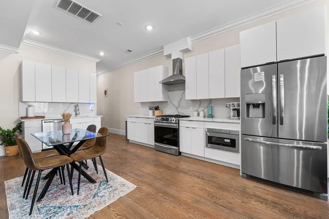 a kitchen with granite countertop a refrigerator oven a sink dishwasher and white cabinets with wooden floor