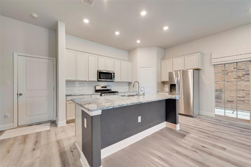 7617 Sunset Boulevard Rowlett, TX 75088 - Photo 6 of 21 Kitchen featuring stainless steel appliances, light stone counters, backsplash, light wood-style floors, and a center island with sink