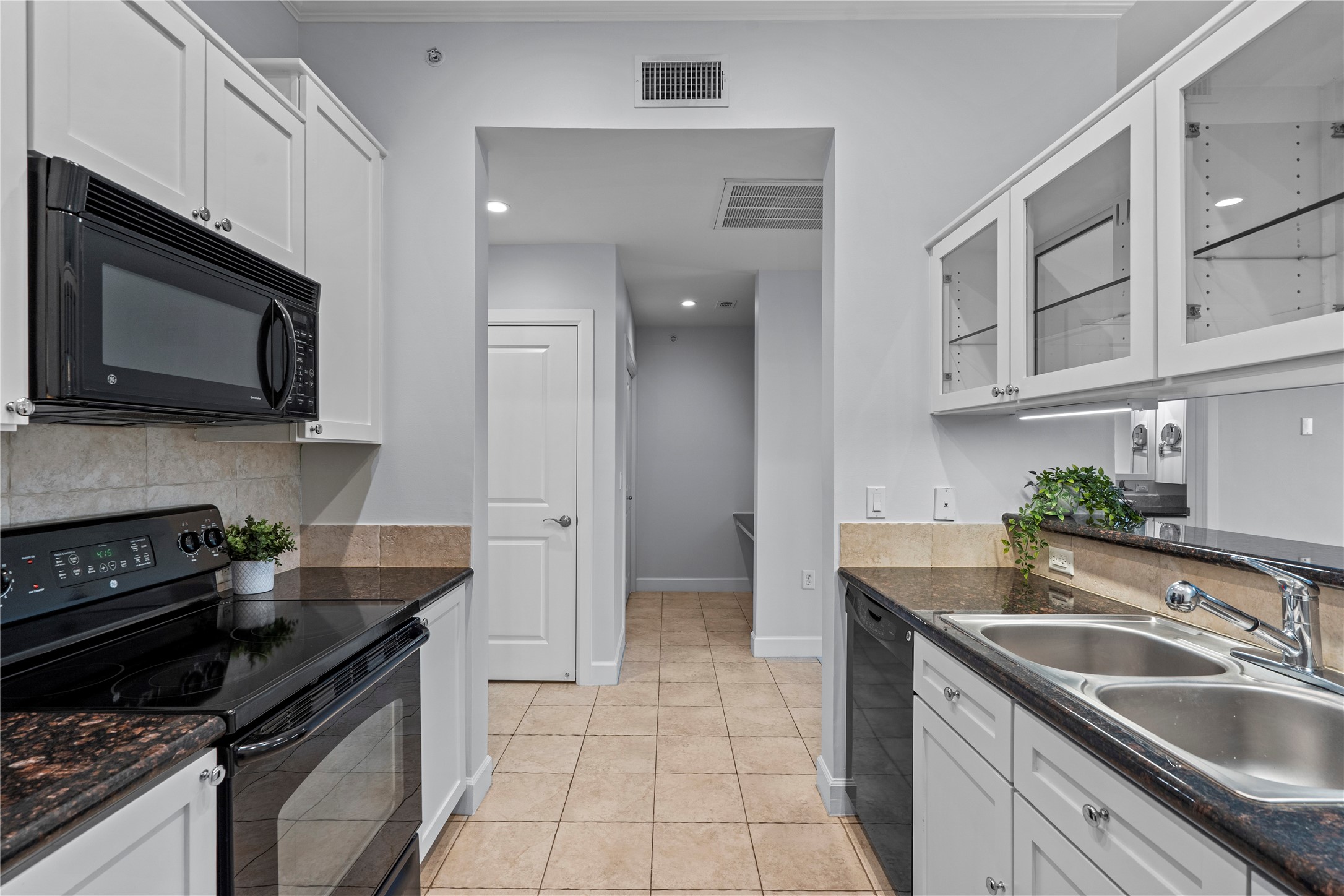 1900 Genesee Street, Unit 203 Houston, TX 77006 - Photo 13 of 30 This kitchen features modern white cabinetry with glass-front accents, sleek black appliances, and a double sink. It has granite countertops and neutral tiled flooring, offering a clean and functional space.