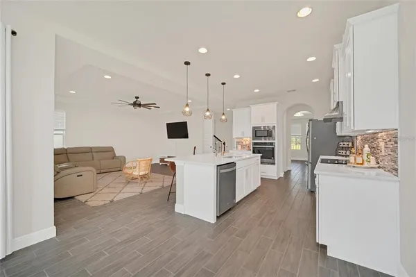 a large living room with stainless steel appliances kitchen island lots of white furniture a wooden floor and a sink
