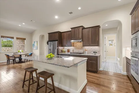 a kitchen with stainless steel appliances granite countertop a stove top oven a sink dishwasher a dining table and chairs with wooden floor