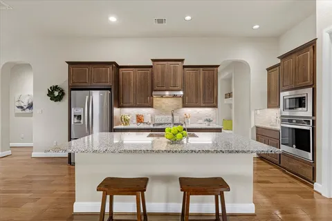 a kitchen with stainless steel appliances granite countertop a refrigerator a stove a sink cabinets and a dining table