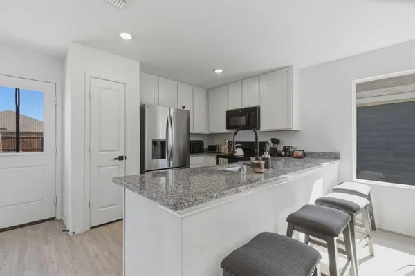 a kitchen with stainless steel appliances granite countertop a sink a stove a refrigerator and a granite counter tops with white cabinets