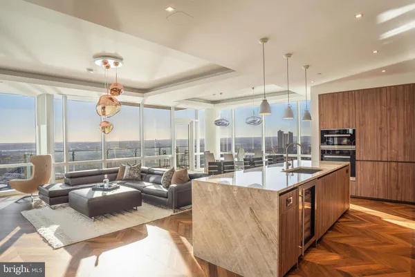 a large kitchen with kitchen island a large counter top a stove a sink a couch and a dining table with wooden floor