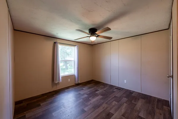 an empty room with wooden floor fan and windows