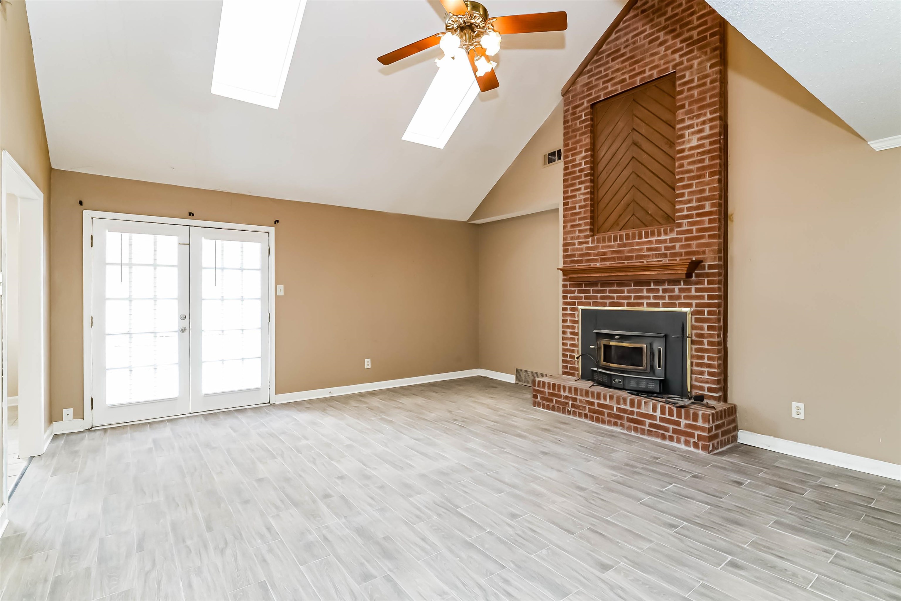 432 Leaf Trail Lane Memphis, TN 38018 - Photo 3 of 17 Unfurnished living room with a wood stove, a skylight, high vaulted ceiling, brick wall, and ceiling fan