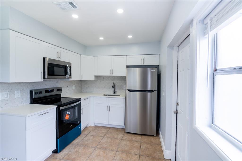 1940 48th Street Southwest Naples, FL 34116 - Photo 15 of 33 Kitchen featuring white shaker-style cabinetry, stainless steel appliances, light-colored countertops, a mosaic tile backsplash, and tile flooring