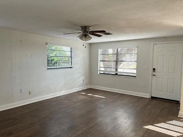an empty room with wooden floor chandelier fan and windows