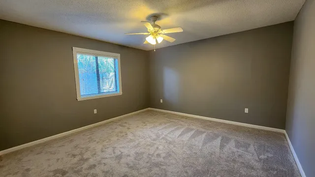 an empty room with windows and chandelier fan
