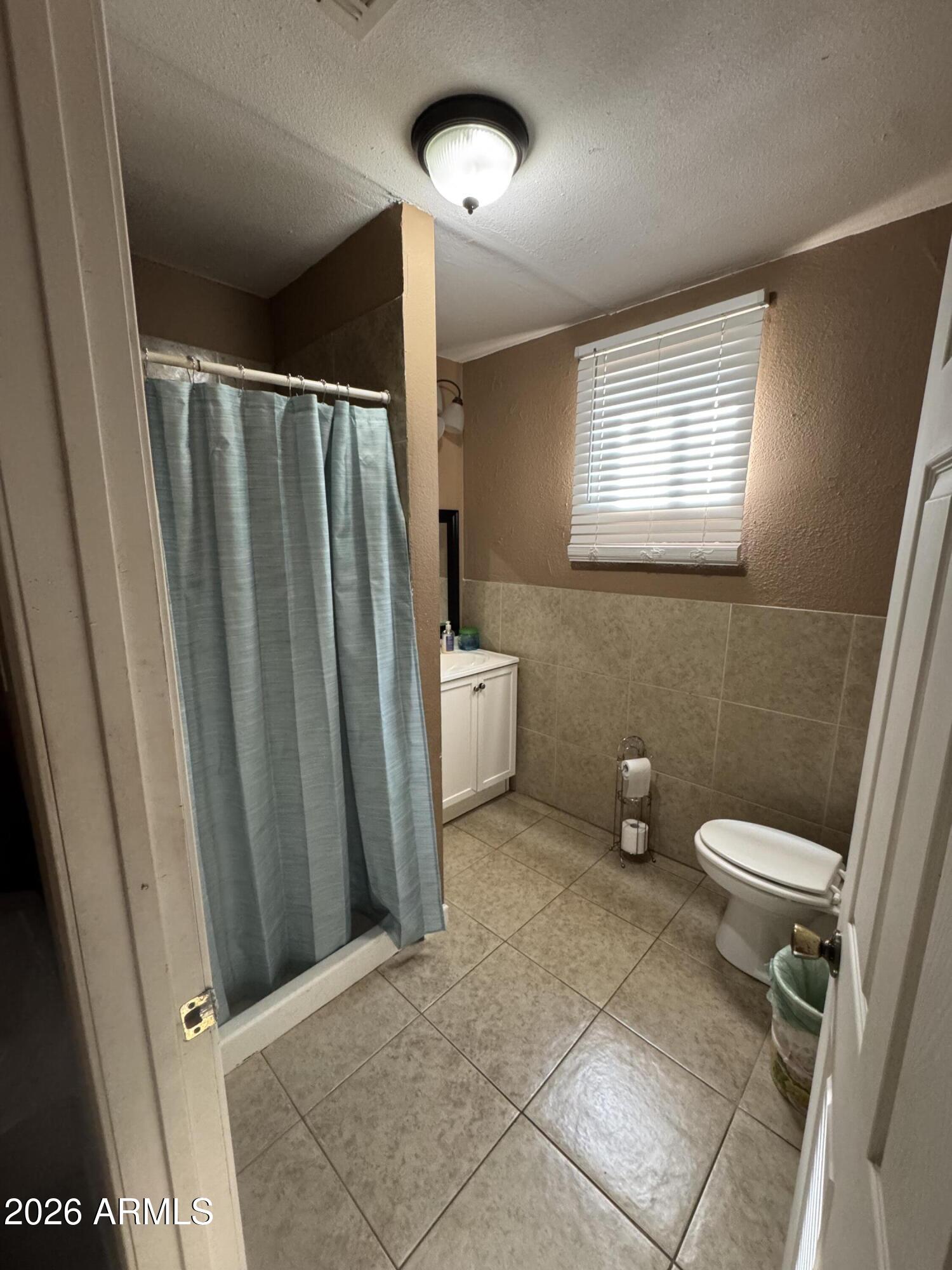 6313 West Osborn Road Phoenix, AZ 85033 - Photo 7 of 12 a bathroom with a toilet a sink a mirror and a window