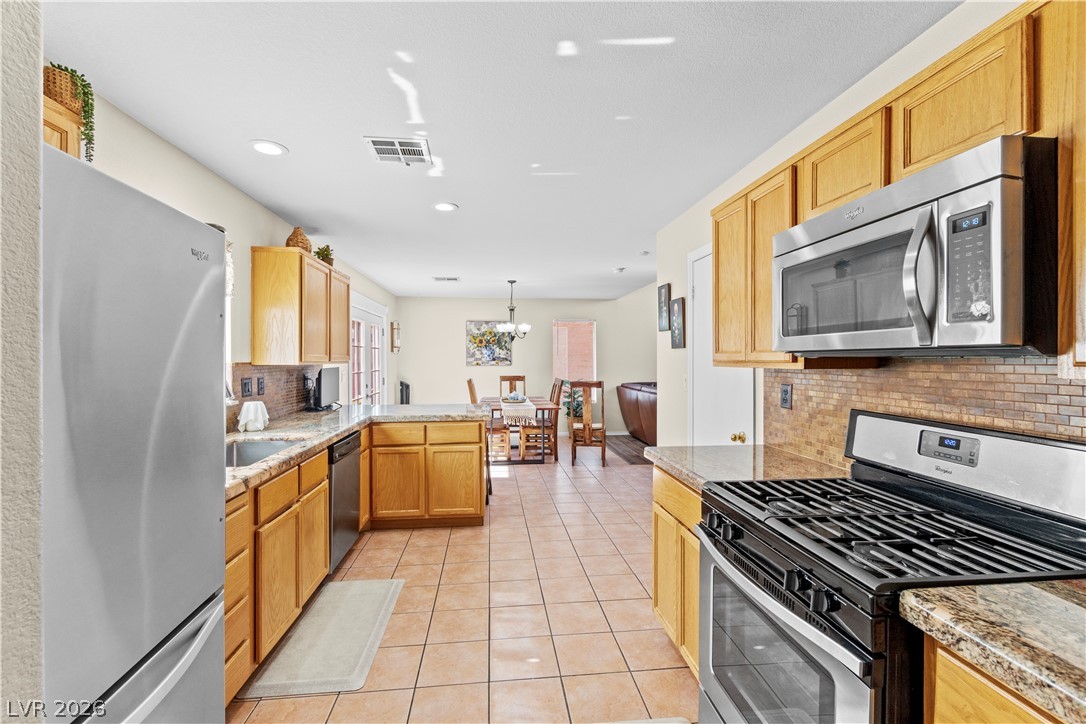 1419 Red Sunset Avenue Henderson, NV 89074 - Photo 11 of 35 Kitchen with stainless steel appliances, a peninsula, light tile patterned floors, light stone counters, and hanging light fixtures