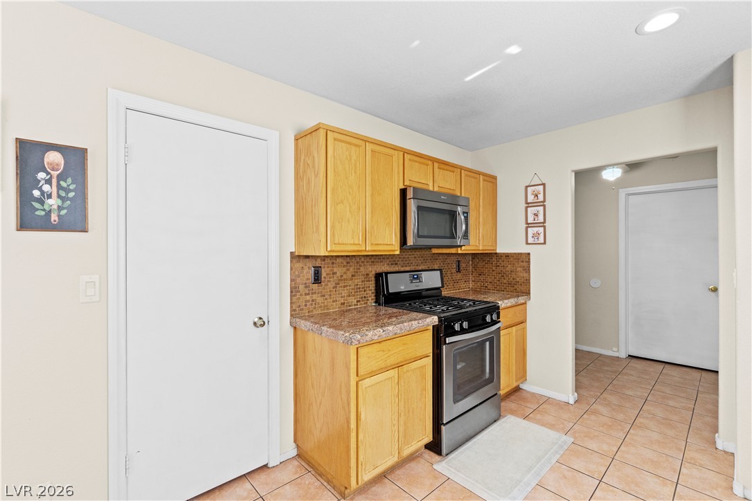 1419 Red Sunset Avenue Henderson, NV 89074 - Photo 14 of 35 Kitchen with stainless steel appliances, tasteful backsplash, light tile patterned flooring, and light wood finish cabinets