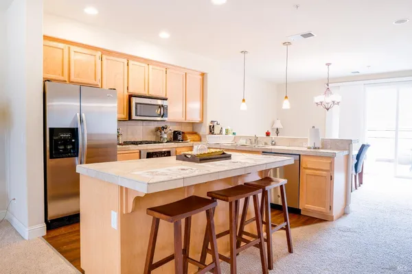 a kitchen with stainless steel appliances kitchen island granite countertop a sink a stove a refrigerator and island with wooden floor