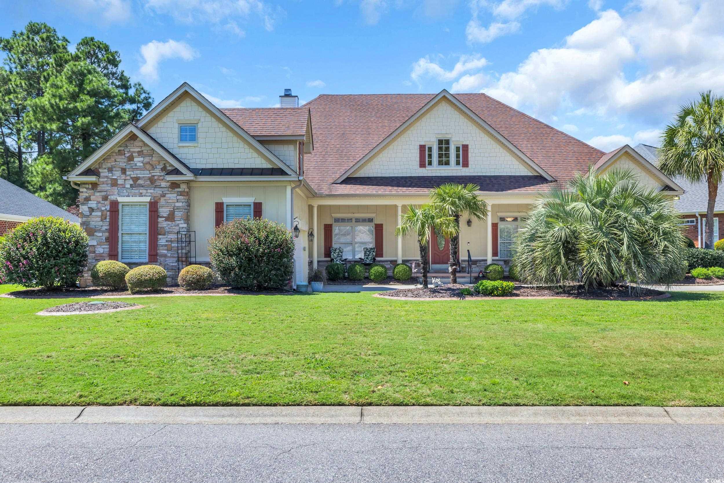 Craftsman-style home with covered porch, a shingled roof, stone siding, a front lawn, and a chimney
