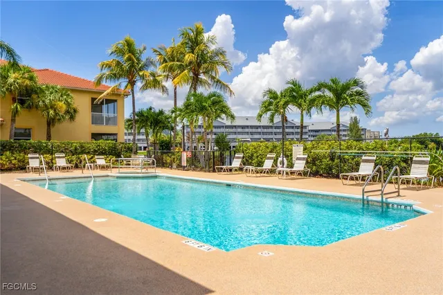 a view of swimming pool with a lawn chairs under palm trees