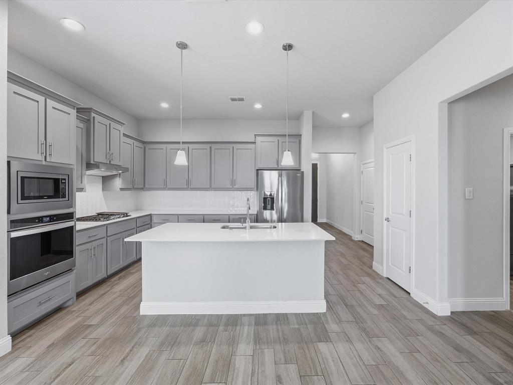 1121 Knightsbridge Road Argyle, TX 76226 - Photo 4 of 39 Modern kitchen featuring gray cabinetry, a central island with dual pendant lighting, stainless steel appliances, white countertops, and wood-finish flooring