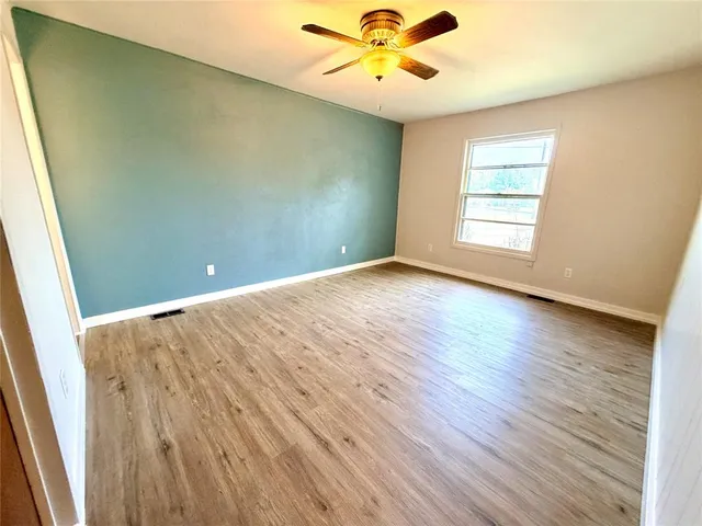 an empty room with wooden floor fan and windows