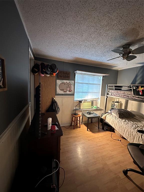 1048 Red Bird Seven Points, TX 75143 - Photo 26 of 30 Bedroom featuring a wainscoted wall, light wood-type flooring, a textured ceiling, wooden walls, and ceiling fan