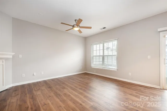 an empty room with wooden floor fan and windows