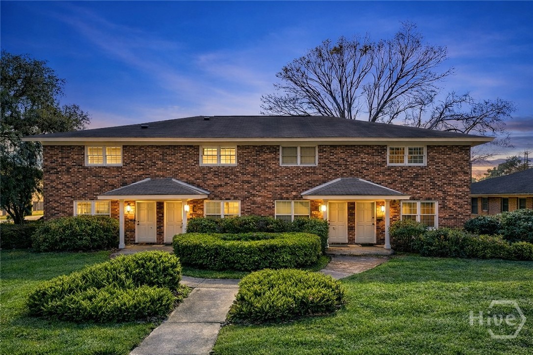 3 Berkley Place Savannah, GA 31405 - Photo 2 of 36 Charming brick townhome with inviting curb appeal, landscaped walkways, and warm exterior lighting at dusk.