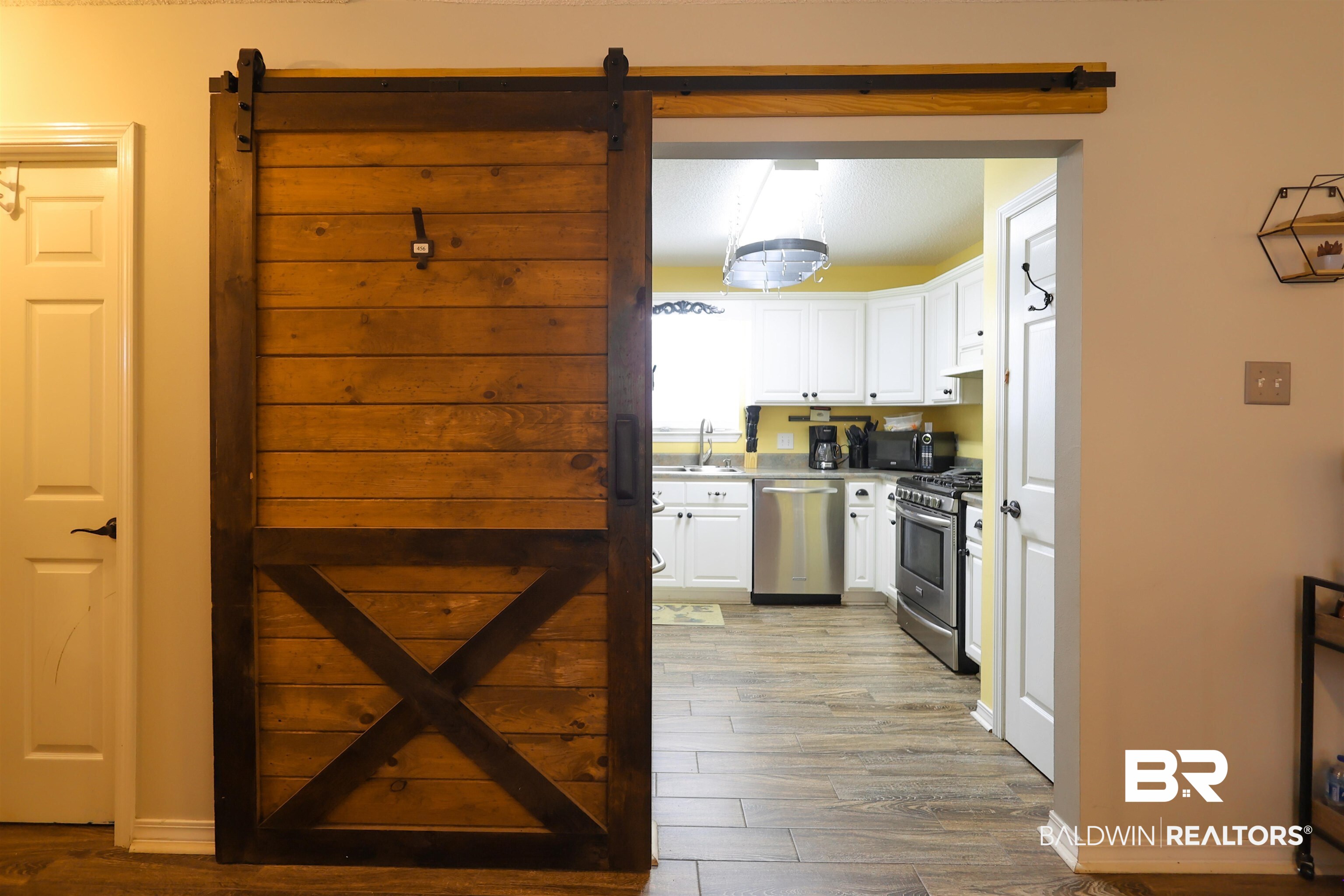 7790 Audubon Drive Foley, AL 36535 - Photo 8 of 39 Barn door entrance to the kitchen featuring wood-finish flooring, white cabinetry, a stainless steel gas range, and a stainless steel dishwasher