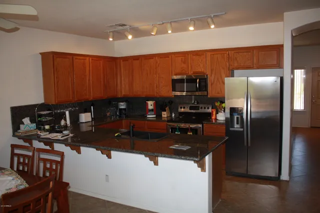 a kitchen with stainless steel appliances granite countertop a refrigerator a stove and a sink with wooden cabinets