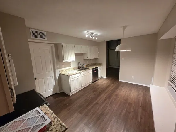 a kitchen with granite countertop a refrigerator oven a sink dishwasher and white cabinets with wooden floor