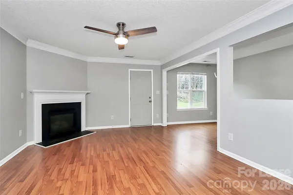 a view of an empty room with wooden floor fireplace and a window
