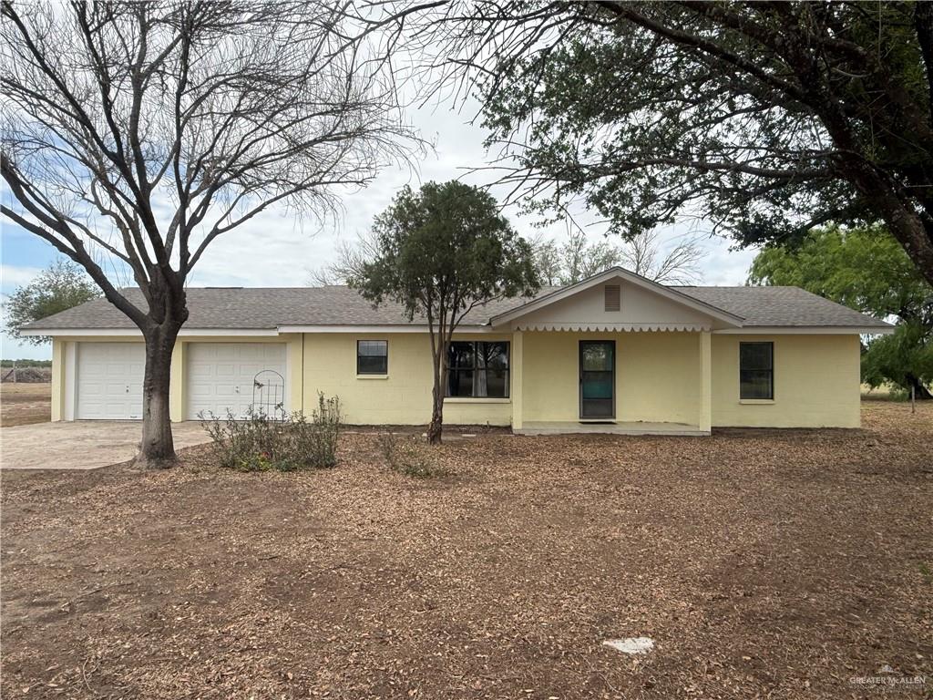 Ranch-style home with a garage, a shingled roof, concrete driveway, and covered porch