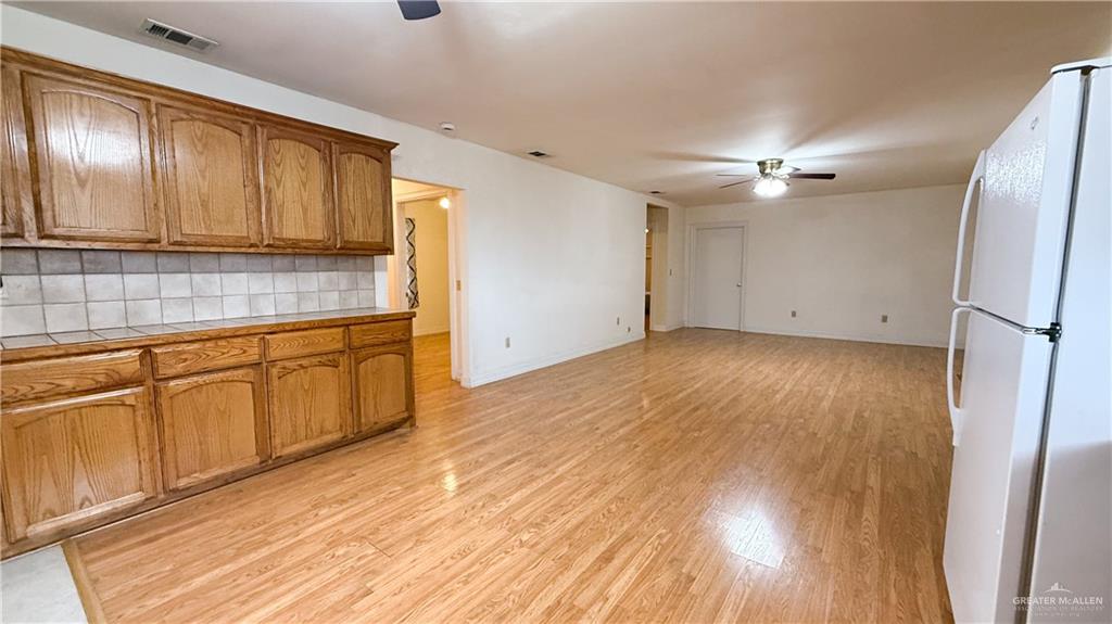21713 North Western Road Edinburg, TX 78541 - Photo 4 of 24 Kitchen with a ceiling fan, freestanding refrigerator, light wood finished floors, wood finish cabinetry, and tasteful backsplash