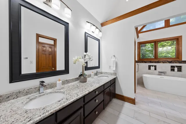 a bathroom with a granite countertop tub a double vanity sink a mirror and a window