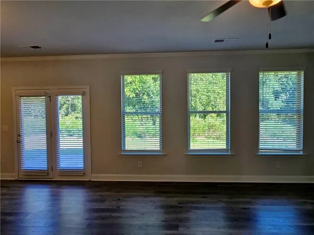 an empty room with windows a fireplace a ceiling fan and wooden floor