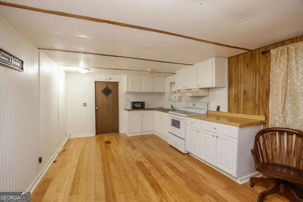 a kitchen with granite countertop a refrigerator a stove a sink and white cabinets with wooden floor