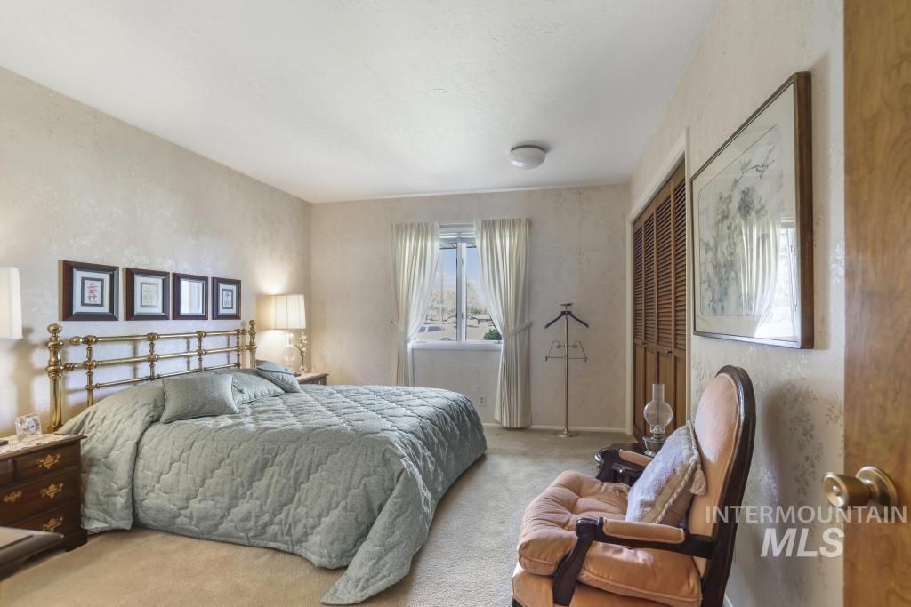 2018 Rancho Vista Drive Twin Falls, ID 83301 - Photo 25 of 50 Carpeted bedroom featuring a brass headboard, a window with curtains, wood-louvered bi-fold closet doors, a ceiling-mounted light fixture, and textured wall finishes
